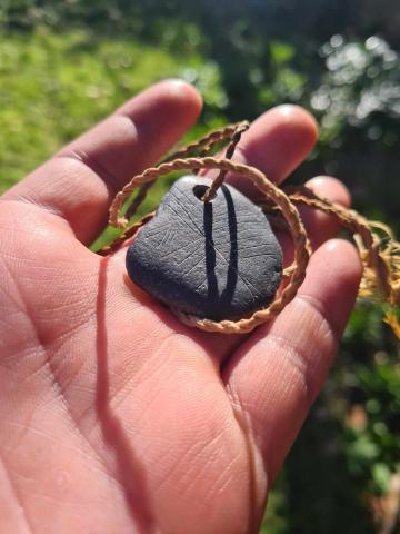 The photo shows a replica of the famous engraved shale pendant from Star Carr. It has been strung with a fine twisted cord made from lime bast.