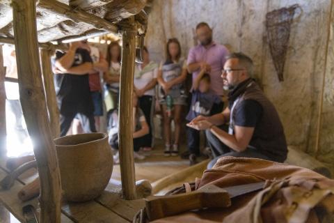 An archaeologist of the museum is showing to the public some replicas of prehistoric tools inside a pile dwelling constructed as in Prehistory