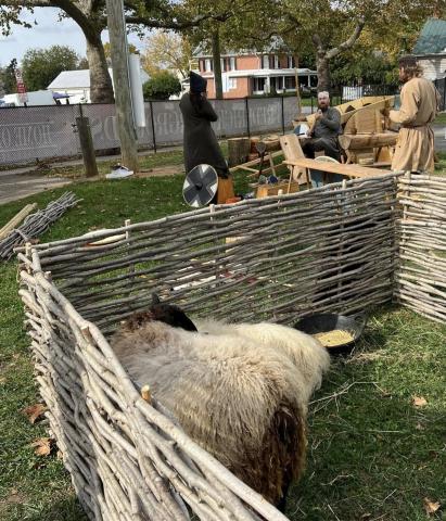 Agriculture A withy fenced enclosure with sheep penned within, ready for shearing.  A few workers hold a discussion amongst their tools, by a cart.