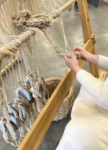 Textile Production A weaver is sitting at the foot of a large warp-weighted loom, chaining the loose ends of the warp threads. Soapstone loom weights are attached to the chained warp, to provide tension.